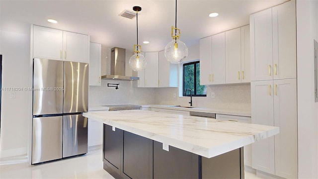 kitchen with sink, stainless steel refrigerator, pendant lighting, wall chimney range hood, and white cabinets