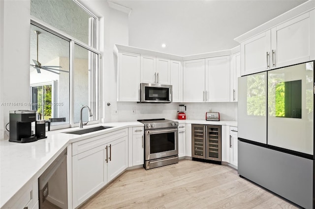 kitchen with light wood-type flooring, stainless steel appliances, sink, white cabinets, and wine cooler