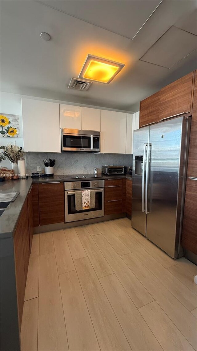 kitchen featuring kitchen peninsula, appliances with stainless steel finishes, tasteful backsplash, sink, and light hardwood / wood-style floors