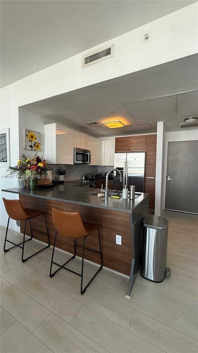 kitchen with decorative backsplash, white cabinetry, light hardwood / wood-style flooring, and appliances with stainless steel finishes