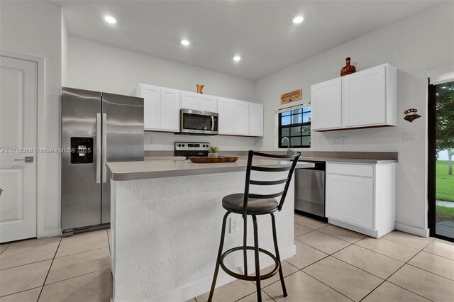 kitchen with white cabinetry, a kitchen island, light tile patterned floors, and appliances with stainless steel finishes