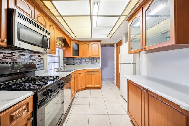 kitchen featuring decorative backsplash, sink, black gas range, white fridge, and light tile patterned flooring