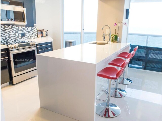 kitchen featuring backsplash, a water view, sink, appliances with stainless steel finishes, and a breakfast bar area