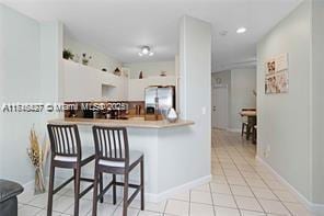 kitchen featuring stainless steel refrigerator with ice dispenser, light tile patterned floors, white cabinetry, a kitchen bar, and kitchen peninsula