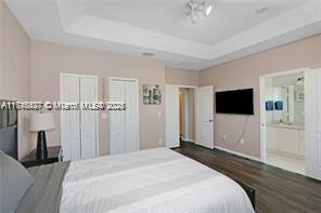 bedroom featuring a raised ceiling, connected bathroom, dark hardwood / wood-style flooring, and two closets