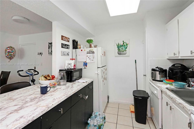 kitchen with a skylight, light tile patterned flooring, white appliances, decorative backsplash, and white cabinets