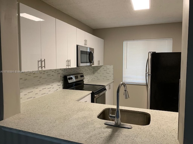 kitchen with light stone countertops, appliances with stainless steel finishes, backsplash, sink, and white cabinetry