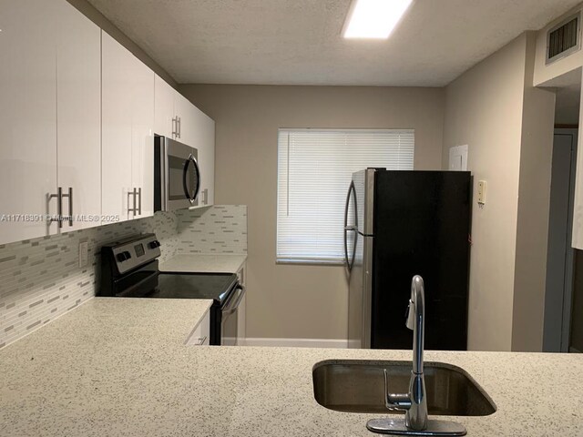 kitchen featuring backsplash, white cabinets, sink, light stone countertops, and stainless steel appliances