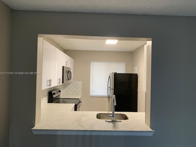 kitchen featuring light stone countertops, sink, a textured ceiling, white cabinets, and appliances with stainless steel finishes