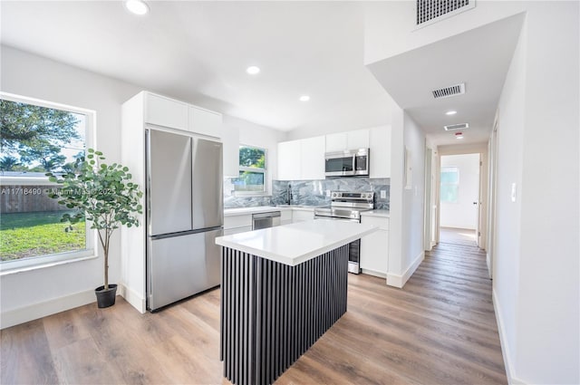 kitchen with appliances with stainless steel finishes, backsplash, a wealth of natural light, white cabinets, and a center island