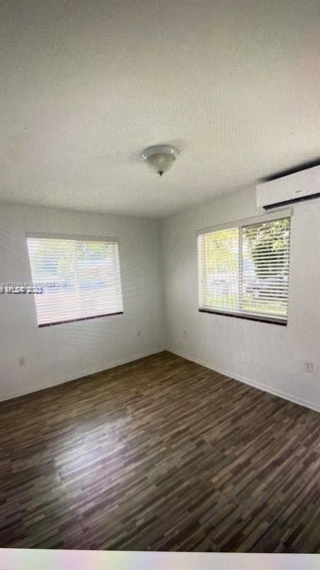 unfurnished room featuring a wall mounted AC, a healthy amount of sunlight, and dark wood-type flooring