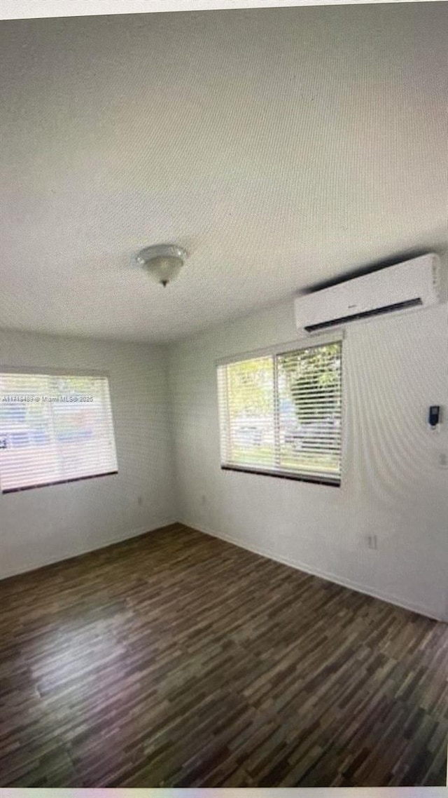 empty room with an AC wall unit and dark wood-type flooring