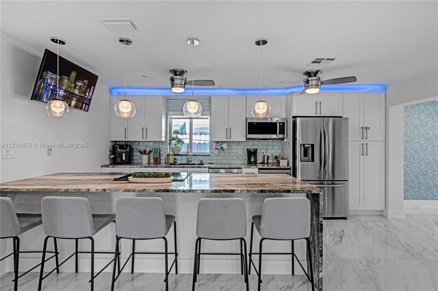 kitchen featuring white cabinets, light stone countertops, appliances with stainless steel finishes, a kitchen island, and a kitchen bar