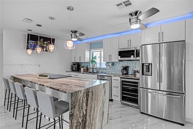 kitchen featuring light stone countertops, wine cooler, stainless steel appliances, and white cabinetry