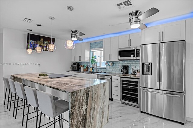 kitchen with light stone countertops, white cabinetry, sink, stainless steel appliances, and wine cooler