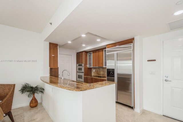 kitchen featuring light stone countertops, sink, stainless steel appliances, backsplash, and kitchen peninsula