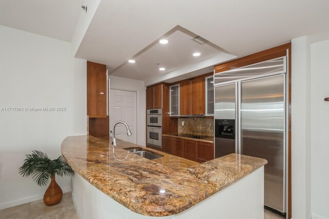 kitchen featuring light stone counters, sink, kitchen peninsula, and stainless steel appliances