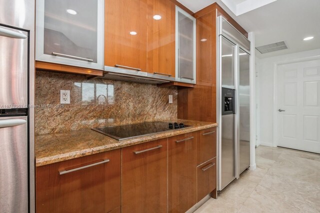 kitchen with stainless steel built in fridge, decorative backsplash, stainless steel fridge, light stone countertops, and black electric cooktop