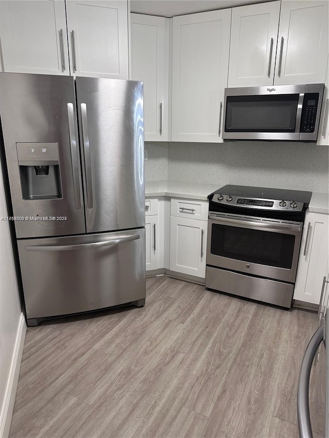 kitchen with tasteful backsplash, white cabinetry, light hardwood / wood-style flooring, and appliances with stainless steel finishes