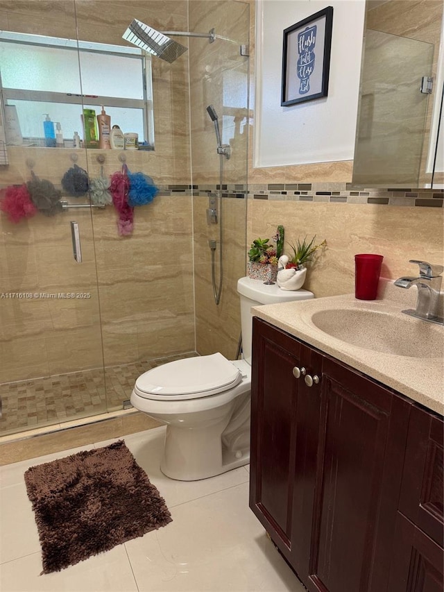 bathroom featuring tile patterned flooring, toilet, vanity, a shower with shower door, and tile walls