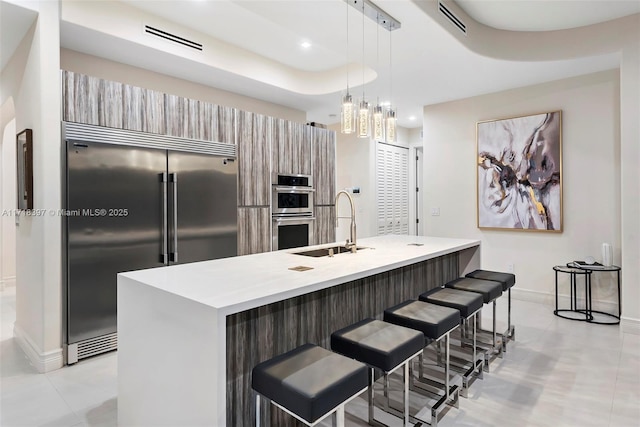 kitchen with sink, a kitchen breakfast bar, an island with sink, pendant lighting, and appliances with stainless steel finishes