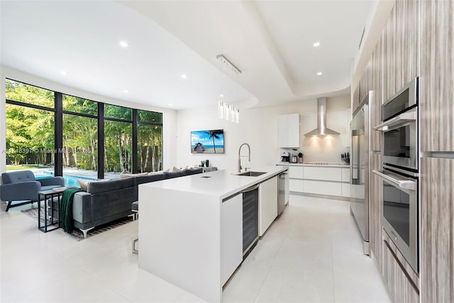 kitchen featuring pendant lighting, a kitchen island with sink, sink, wall chimney exhaust hood, and white cabinetry