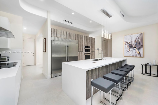 kitchen with a kitchen island with sink, a raised ceiling, stainless steel built in fridge, hanging light fixtures, and black electric cooktop