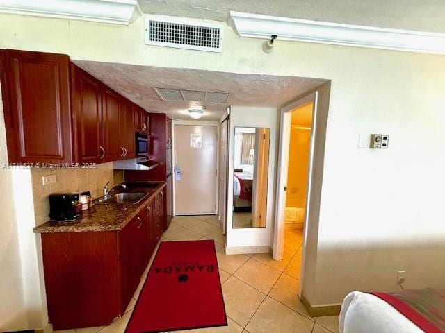 kitchen with dark countertops, visible vents, light tile patterned flooring, a sink, and stainless steel microwave