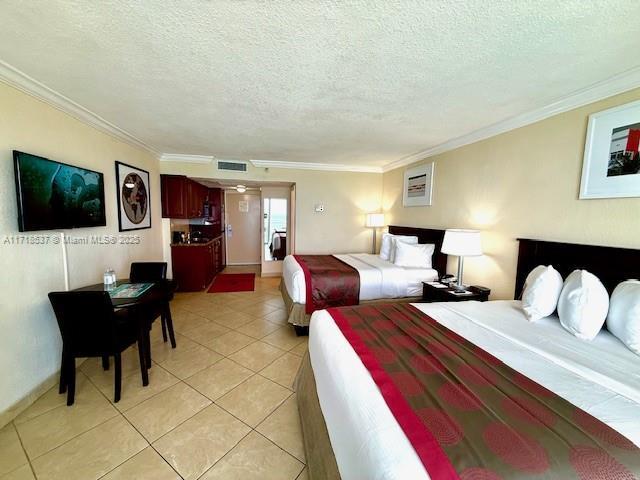 bedroom featuring light tile patterned flooring, visible vents, a textured ceiling, and crown molding