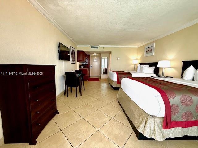 bedroom featuring light tile patterned floors, visible vents, a textured ceiling, and ornamental molding