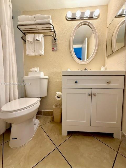 bathroom with toilet, curtained shower, tile patterned flooring, baseboards, and vanity