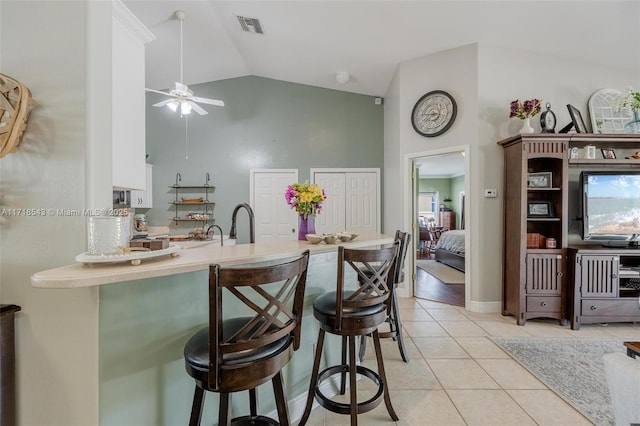 kitchen featuring vaulted ceiling, a breakfast bar, light tile patterned floors, ceiling fan, and kitchen peninsula