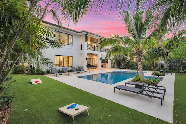 pool at dusk with a patio area and a lawn