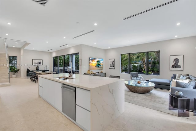 kitchen with light stone countertops, white cabinetry, sink, stainless steel dishwasher, and an island with sink