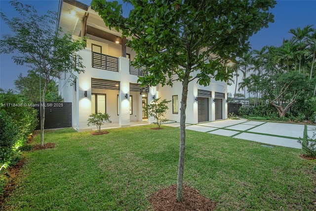 rear view of house featuring a lawn, a balcony, and a garage