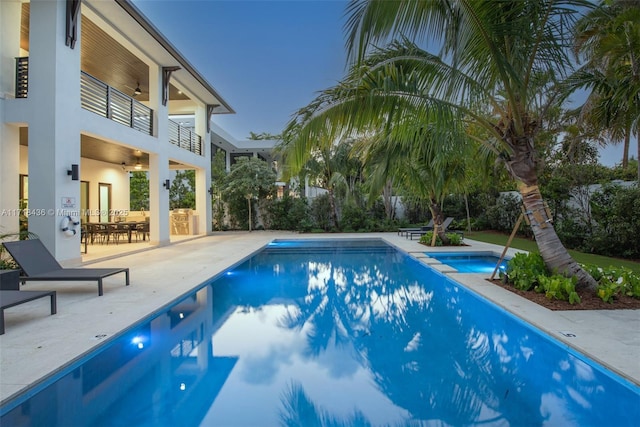 pool at dusk with ceiling fan, a patio area, and an in ground hot tub