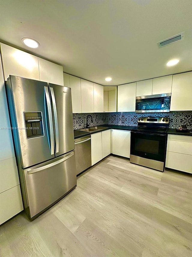 kitchen with decorative backsplash, white cabinetry, stainless steel appliances, and light hardwood / wood-style floors