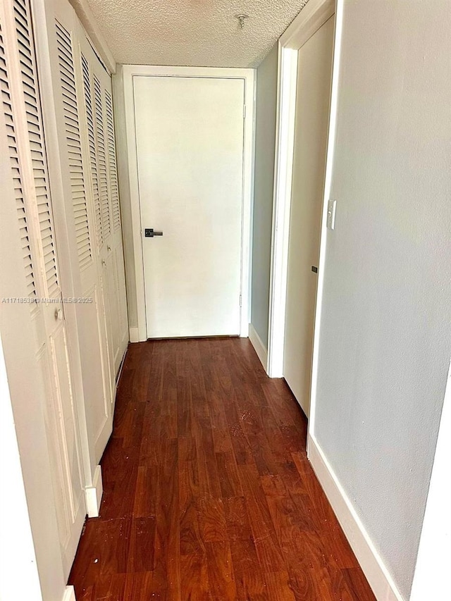 hallway with a textured ceiling and dark wood-type flooring