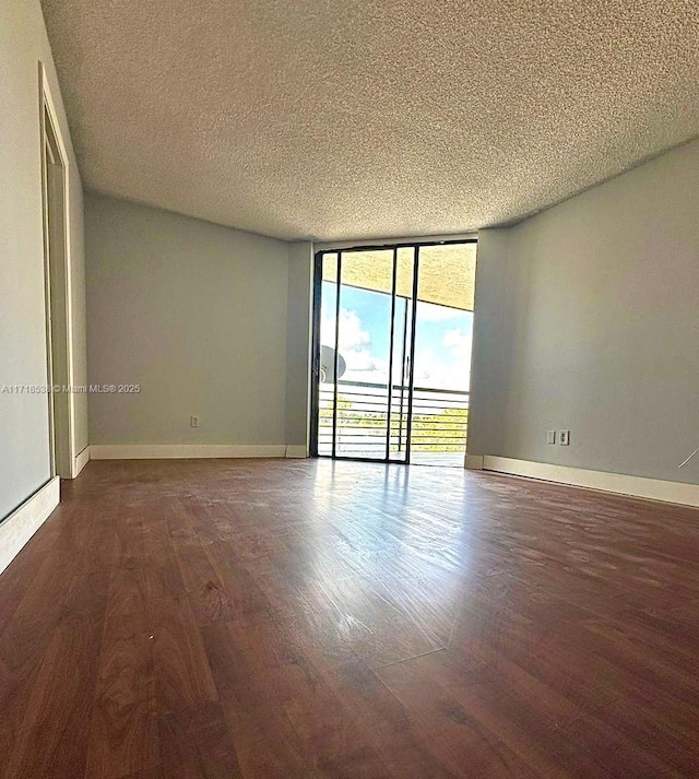 empty room featuring expansive windows, dark hardwood / wood-style flooring, and a textured ceiling