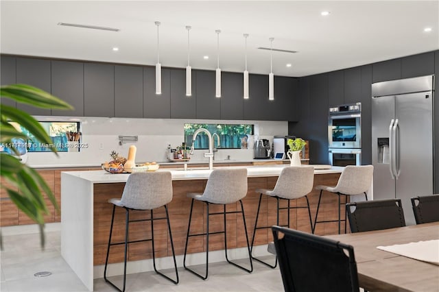 kitchen featuring a kitchen island with sink, a breakfast bar, hanging light fixtures, and appliances with stainless steel finishes