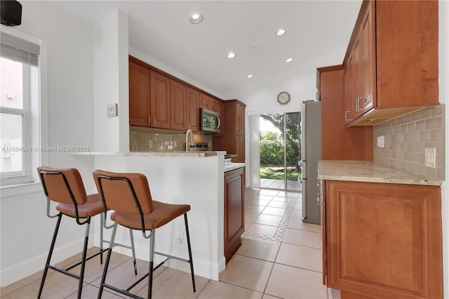 kitchen featuring light stone countertops, lofted ceiling, decorative backsplash, light tile patterned floors, and appliances with stainless steel finishes