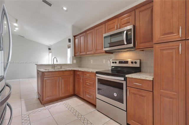 kitchen with kitchen peninsula, appliances with stainless steel finishes, light stone counters, sink, and light tile patterned floors