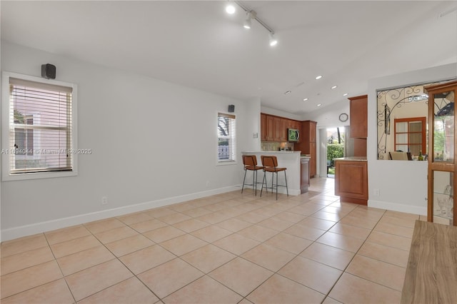 kitchen featuring a healthy amount of sunlight, kitchen peninsula, light tile patterned floors, and vaulted ceiling