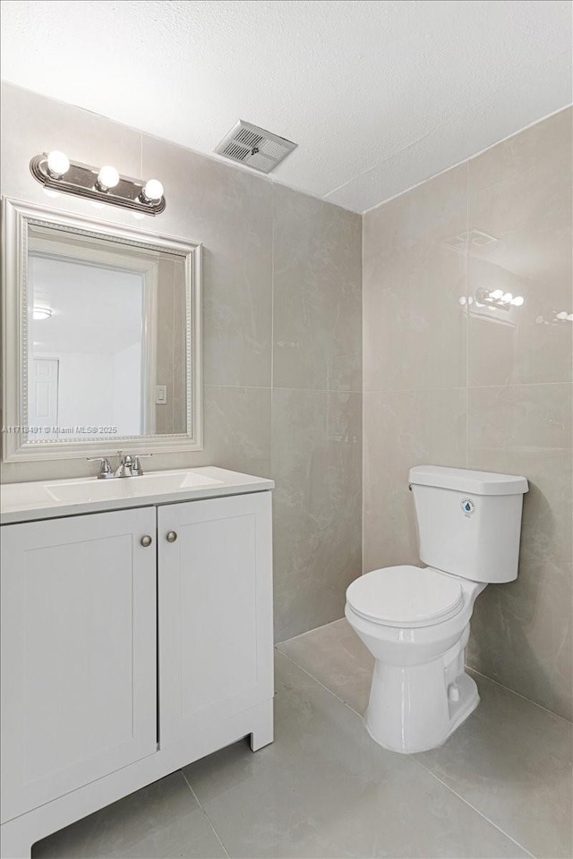 bathroom with tile patterned flooring, a textured ceiling, toilet, vanity, and tile walls