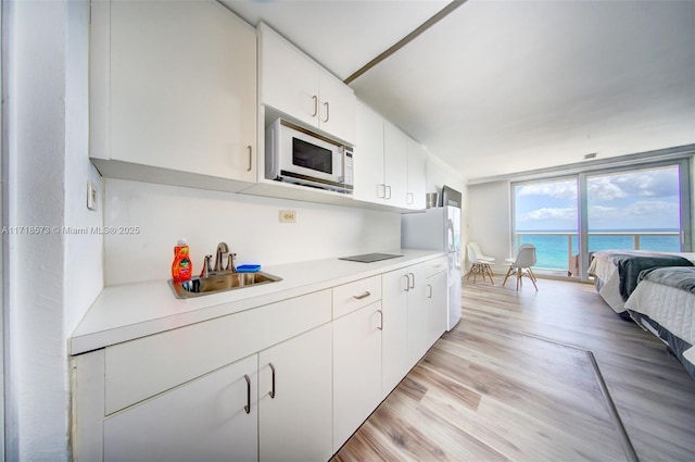 kitchen featuring sink, light hardwood / wood-style floors, white appliances, a water view, and white cabinets