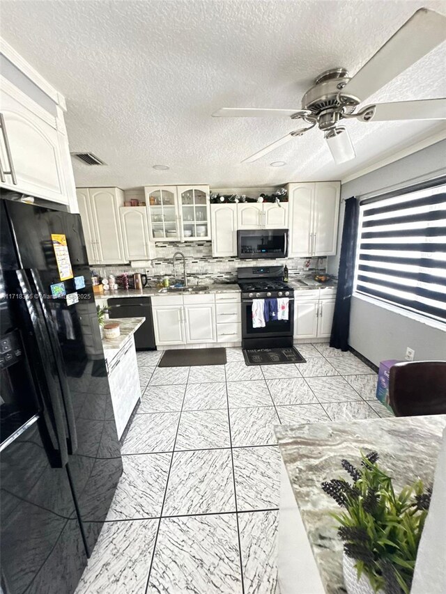 kitchen with gas range, white cabinetry, black fridge, and sink