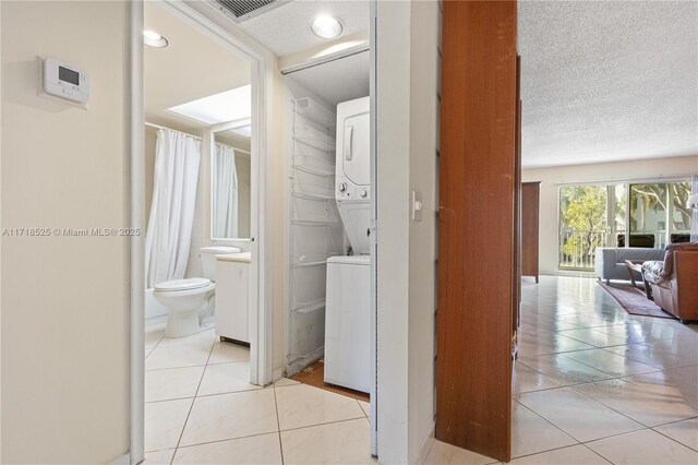 washroom featuring a textured ceiling, stacked washer and clothes dryer, and light tile patterned flooring