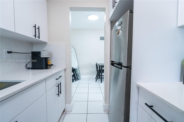 kitchen featuring light stone counters, light tile patterned flooring, stainless steel fridge, decorative backsplash, and white cabinets