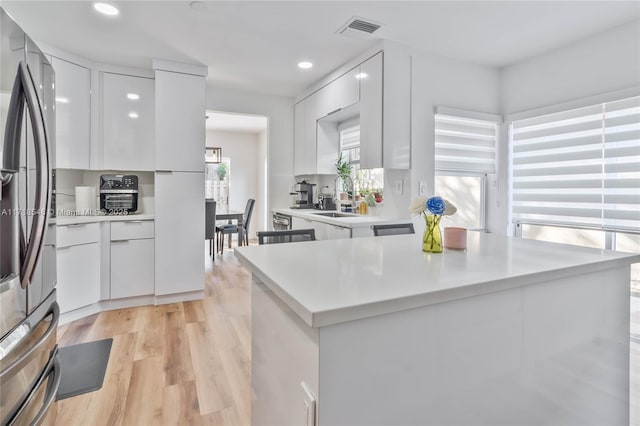 kitchen with stainless steel refrigerator, light hardwood / wood-style flooring, and white cabinets