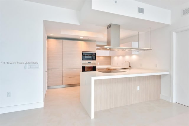 kitchen featuring sink, black electric stovetop, kitchen peninsula, island range hood, and light brown cabinetry